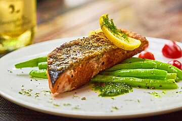 A white plate topped with a piece of salmon and green beans