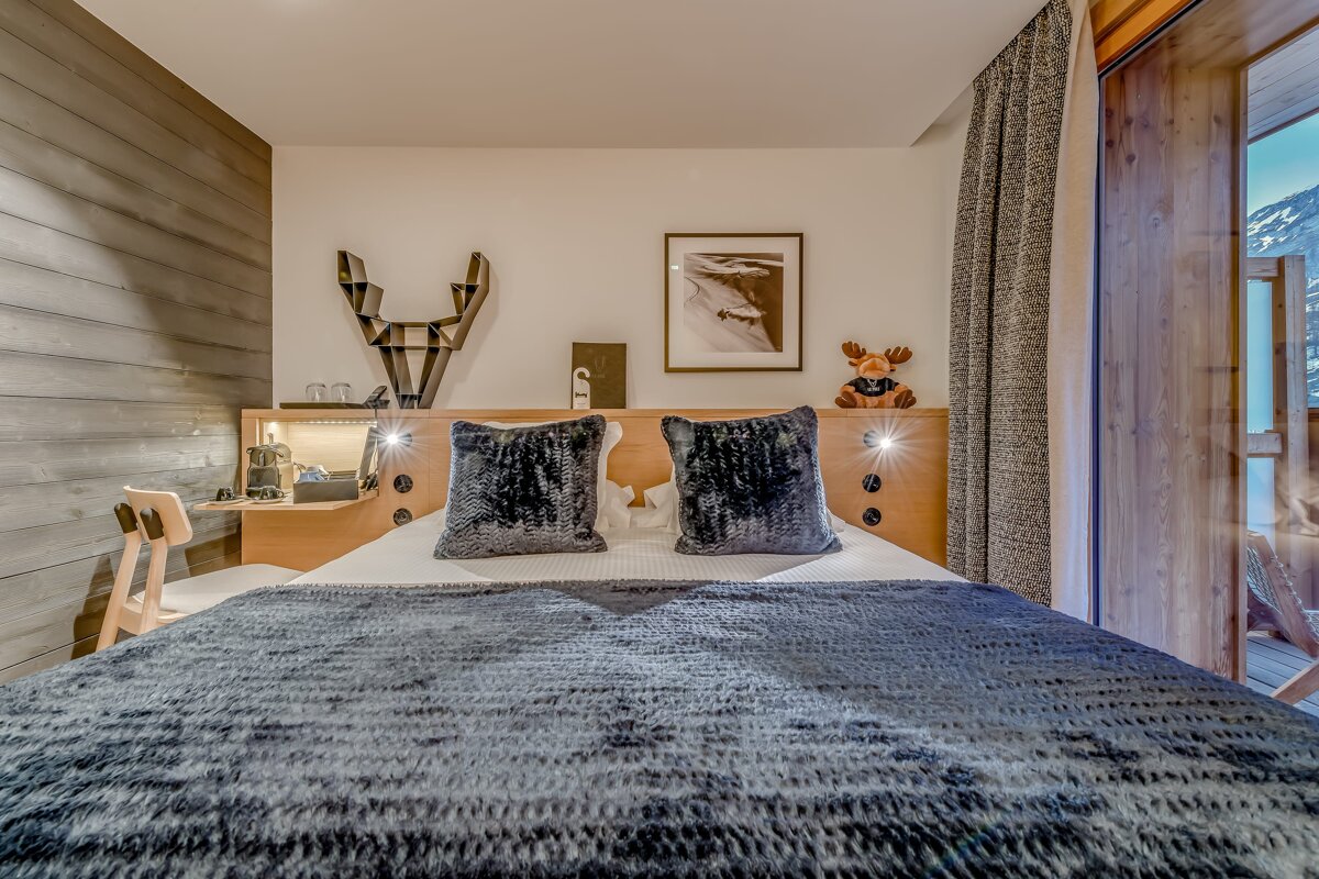 A chic, cozy bedroom with a fluffy bed, wooden headboard, unique antler decor, and a balcony offering a mountain view.