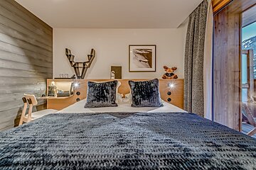 A chic, cozy bedroom with a fluffy bed, wooden headboard, unique antler decor, and a balcony offering a mountain view.