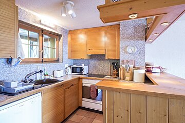 A cozy, rustic kitchen with light wood cabinets, tiled walls, and a wooden breakfast bar.