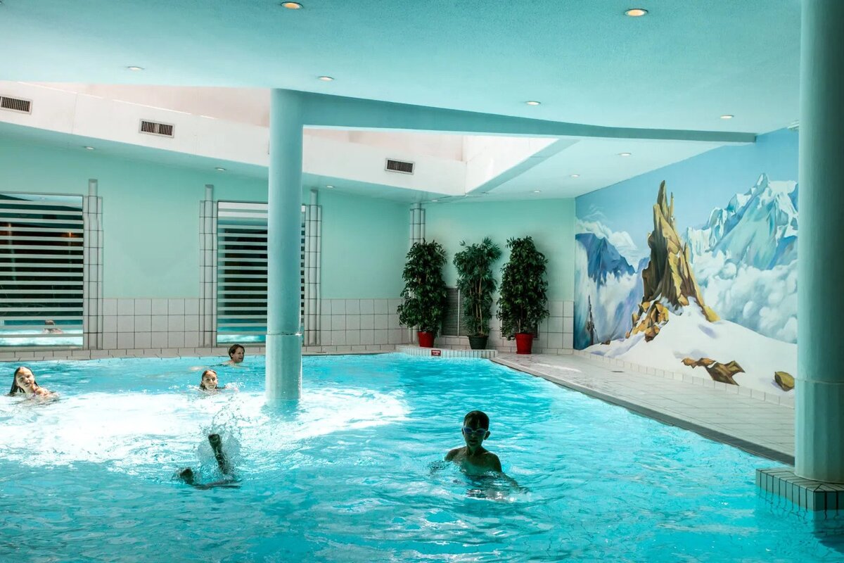 People are swimming in an indoor pool with a painting of mountains on the wall