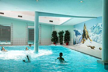 People are swimming in an indoor pool with a painting of mountains on the wall