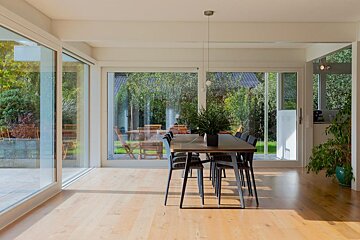 A dining room with a table and chairs and lots of windows