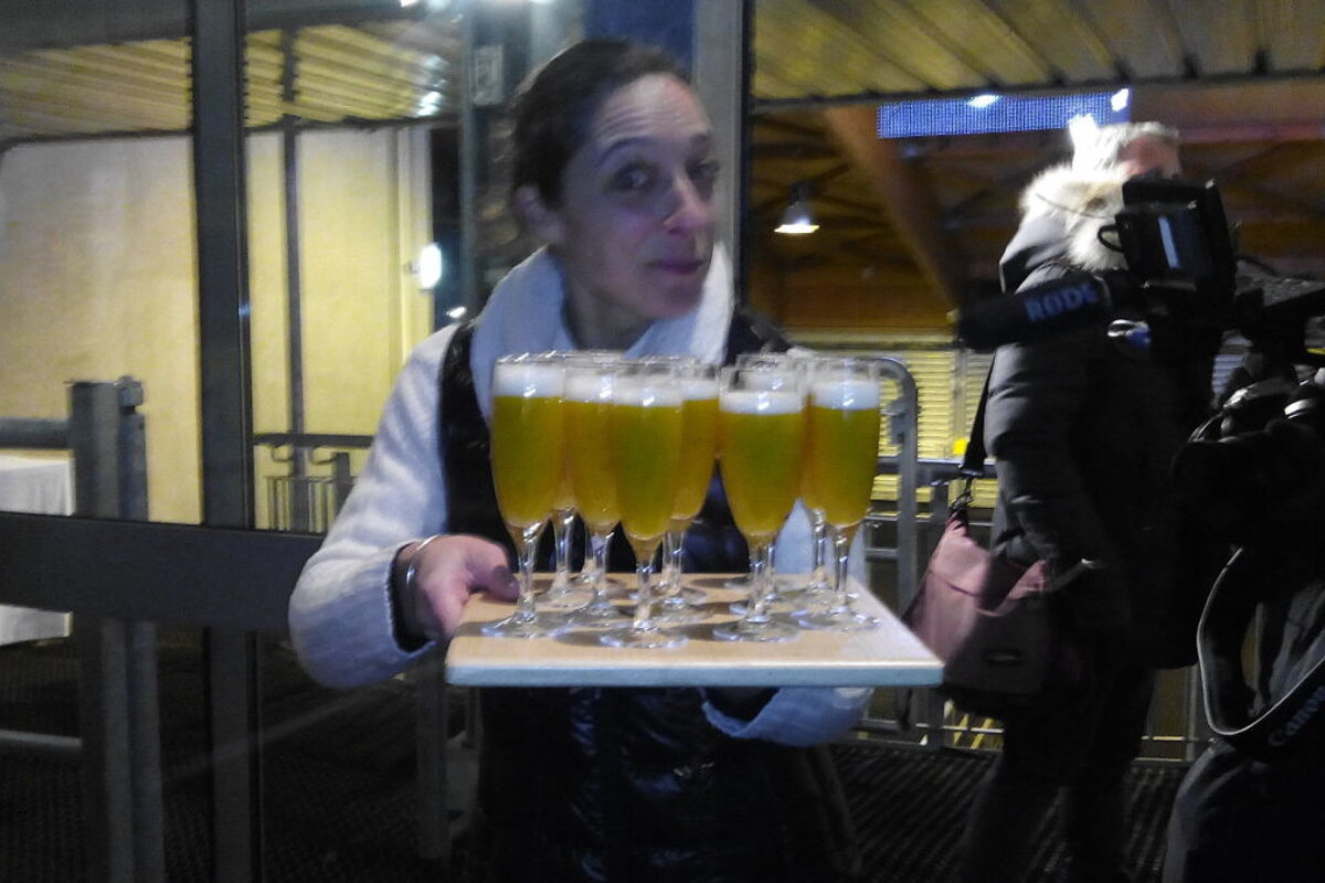 Waitress holding a tray of cocktails in champagne glasses, with a camera crew behind