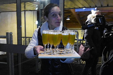 Waitress holding a tray of cocktails in champagne glasses, with a camera crew behind