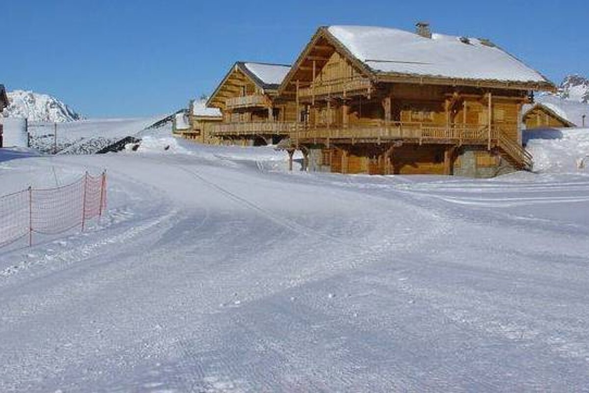 A row of wooden cabins covered in snow on top of a snow covered slope