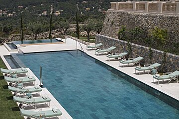 A large swimming pool surrounded by chairs and a stone wall