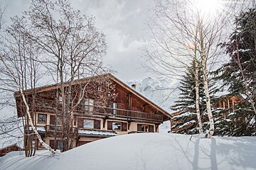 A large wooden house sits on top of a snow covered hill