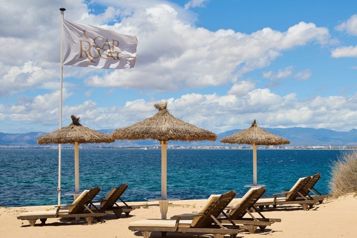 A beach with chairs and umbrellas and a flag that says cap roca