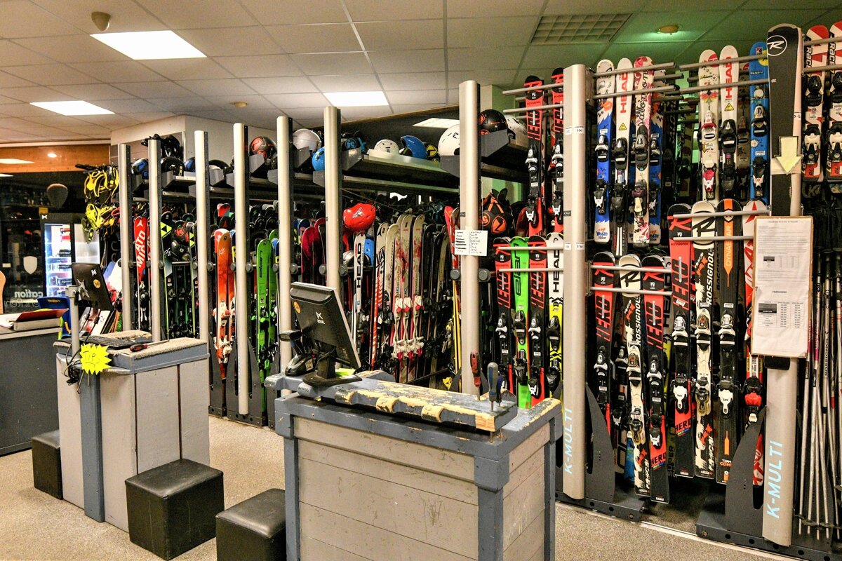A bustling ski shop interior features rows of colorful skis and helmets on display racks, with multiple service counters for customers.