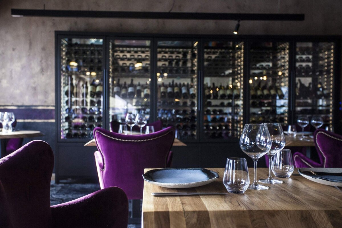 A restaurant with purple chairs and a wall of wine bottles