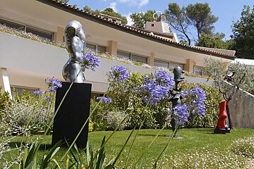 A statue in a garden with purple flowers in front of a building