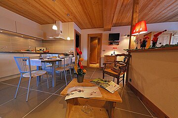 A cozy, open-plan living space with a modern kitchen, dining area, and living room. Features warm wooden ceilings, tiled floors, and inviting decor.