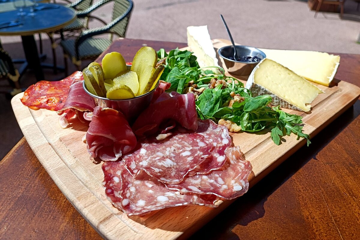 A wooden cutting board with a variety of meats and pickles on it