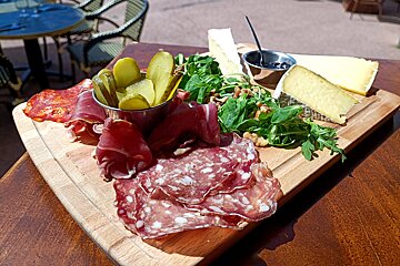 A wooden cutting board with a variety of meats and pickles on it