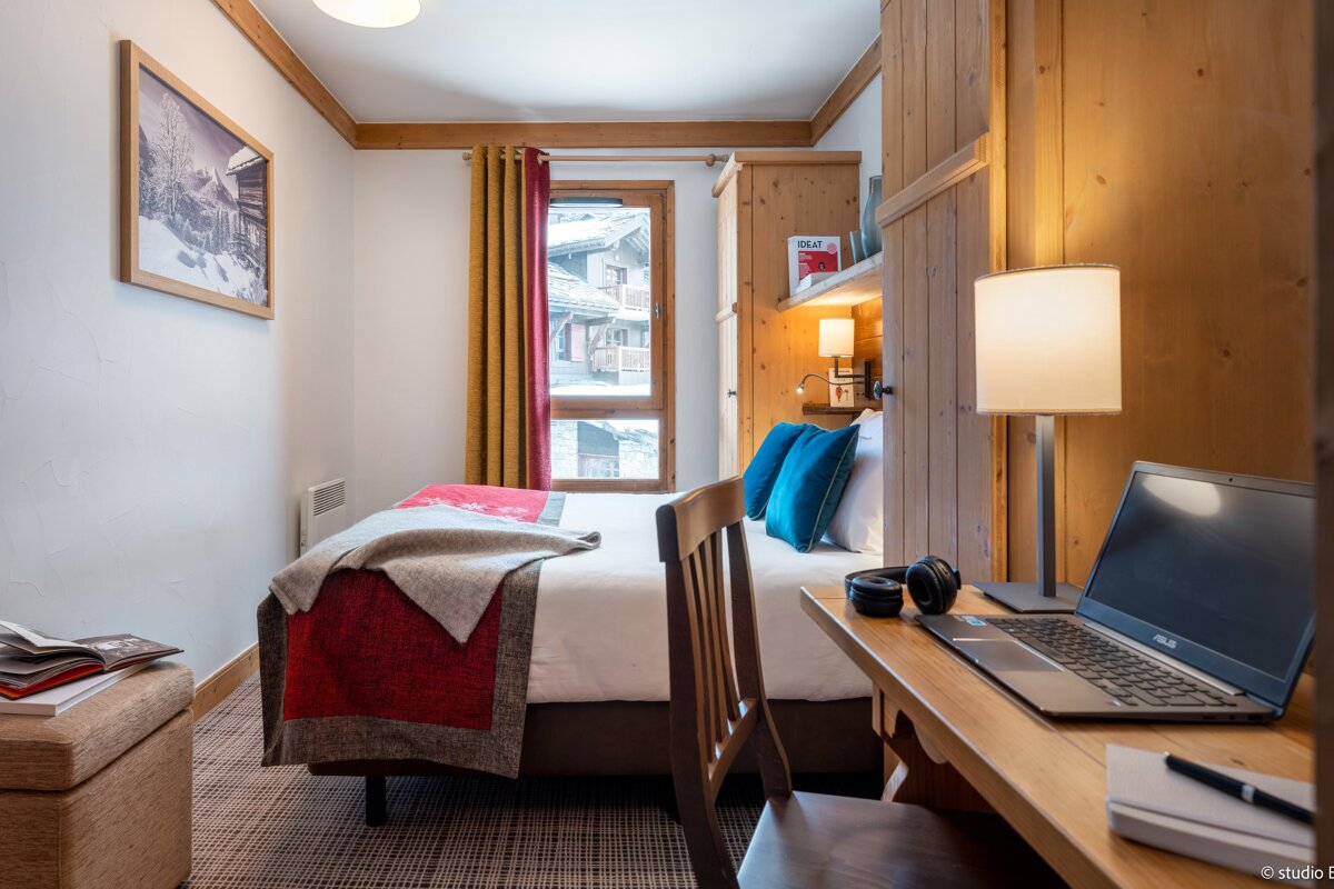 A bedroom with a bed and a desk with an asus laptop on it