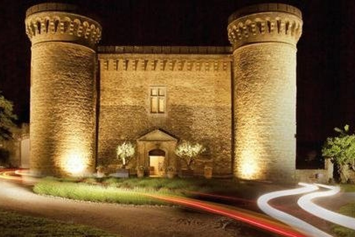 Small castle building with two corner towers at nights with delayed car headlights