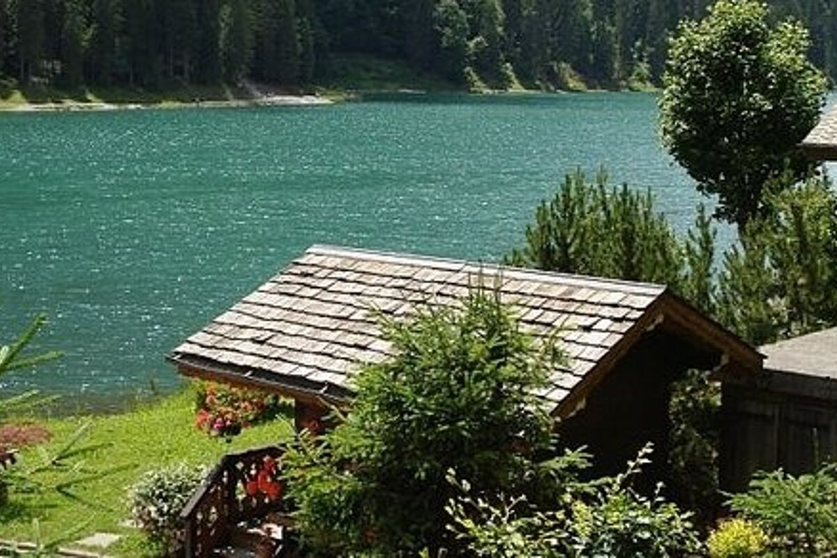 image of a large lake with the roof top of a building and the building in the foreground, green grass on the edge of the lake