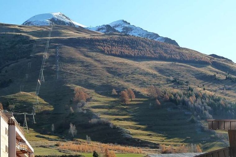 image of a mountain face in the summer with green grass and trees and snow on the mountain peaks at the top