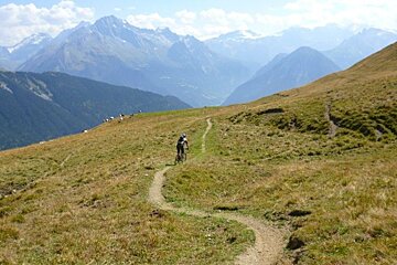 a picture of a lone mountain biker on an open trail in the mountains