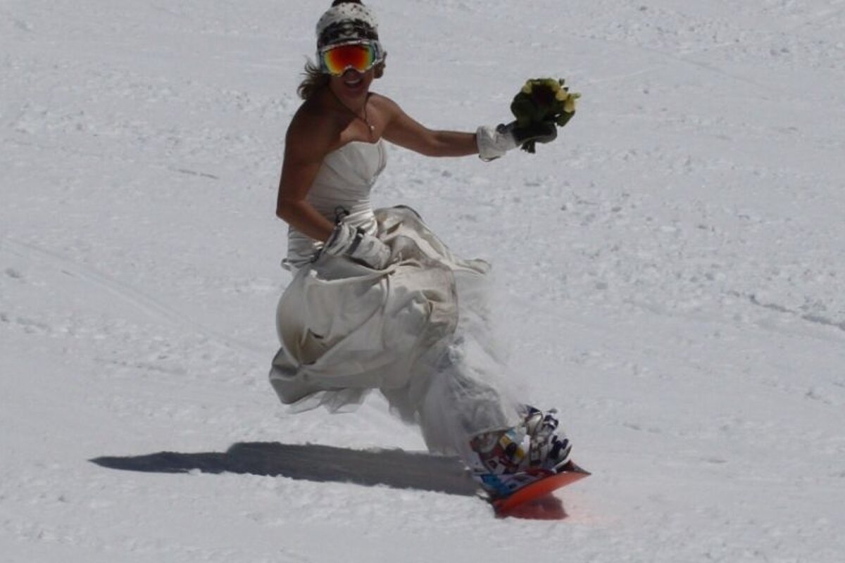 A woman in a wedding dress is snowboarding in the snow