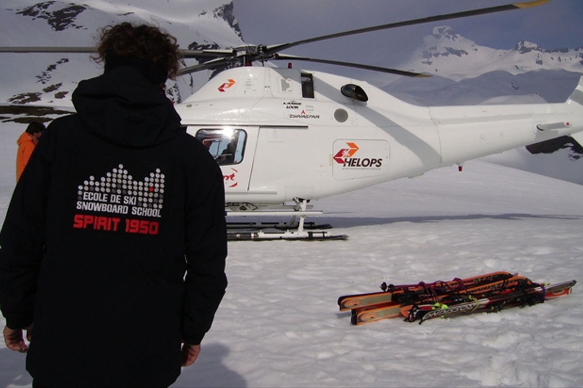 a picture of a mountain guide in a branded jacket near a helicopter