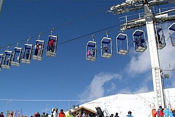 Skiers on a ski lift with the letter r on the pole