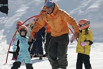 a picture of a man in an orange jacket with 2 kids in ski gear
