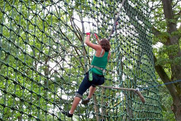 image of a woman climbing a rope fence with a harness on in the forest
