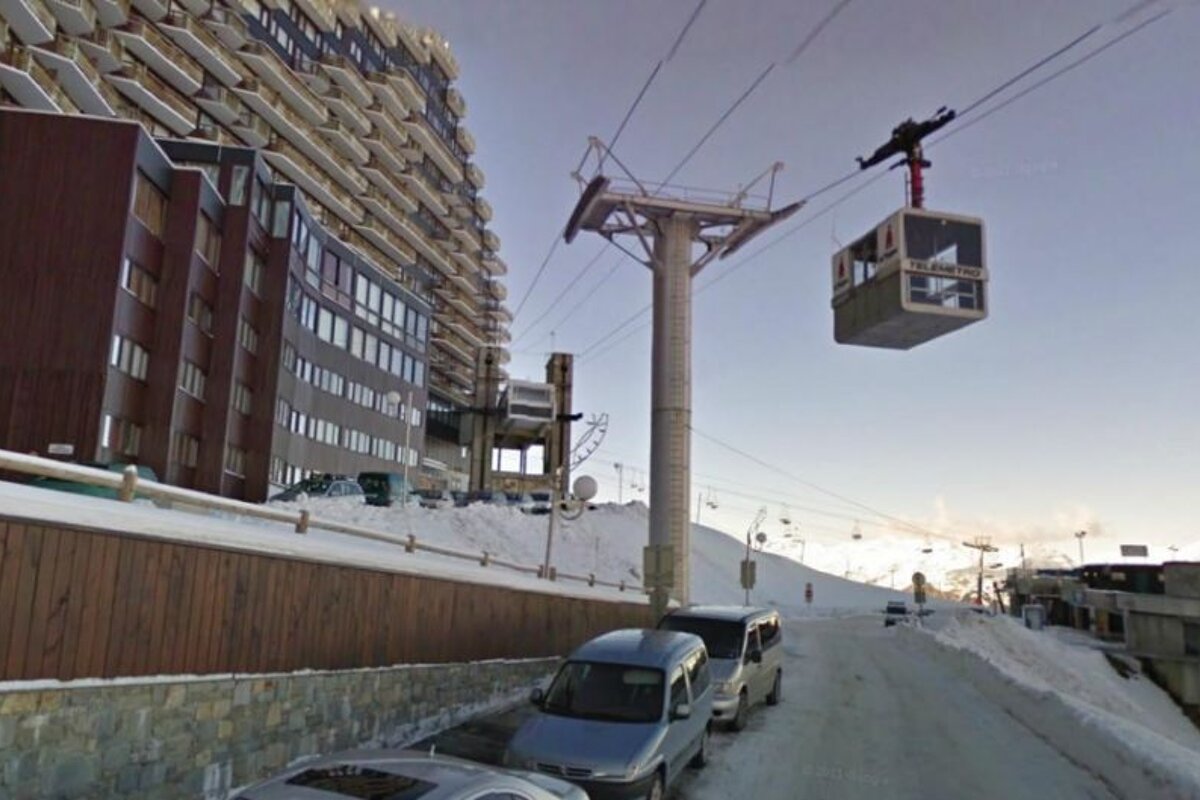 image of a large apartment block/building with a cable car runnning into it and cars parked out front, with chairlifts in the background