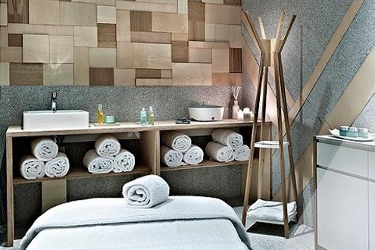 image of a treatment room with a theapy bed and white towels on with sink and shelving with white towels