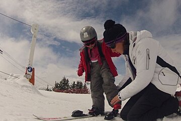 a picture of a female ski instructor helping a small kid with ski boots