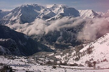 A snowy landscape with mountains and clouds in the background