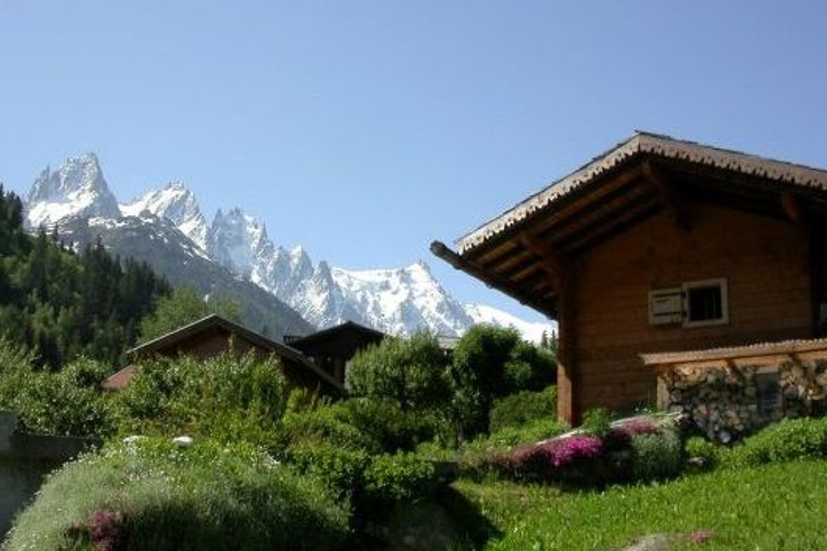 image of a green mountains and some chalet style buildings with snow covered mountains peaks behind in the background