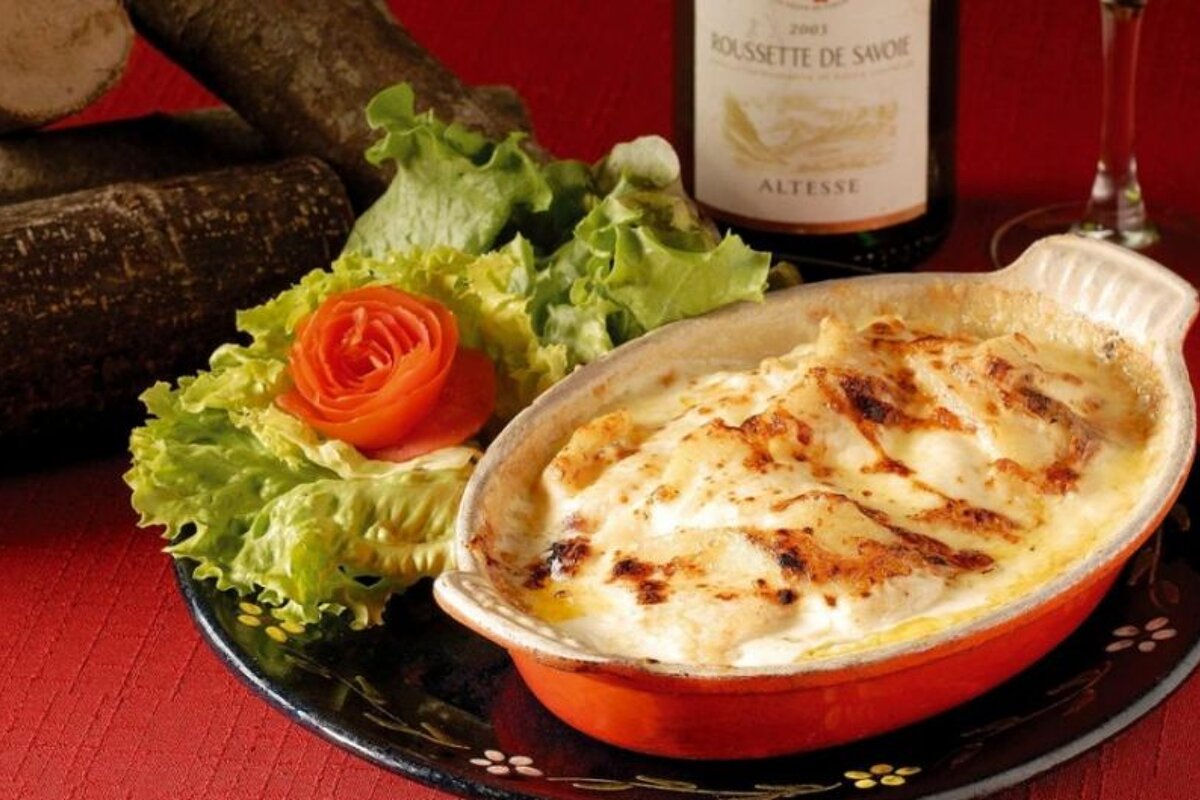 Image of a tartiflette on a plate with salad and a bottle of wine in the background