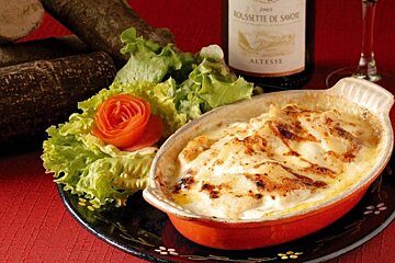 Image of a tartiflette on a plate with salad and a bottle of wine in the background