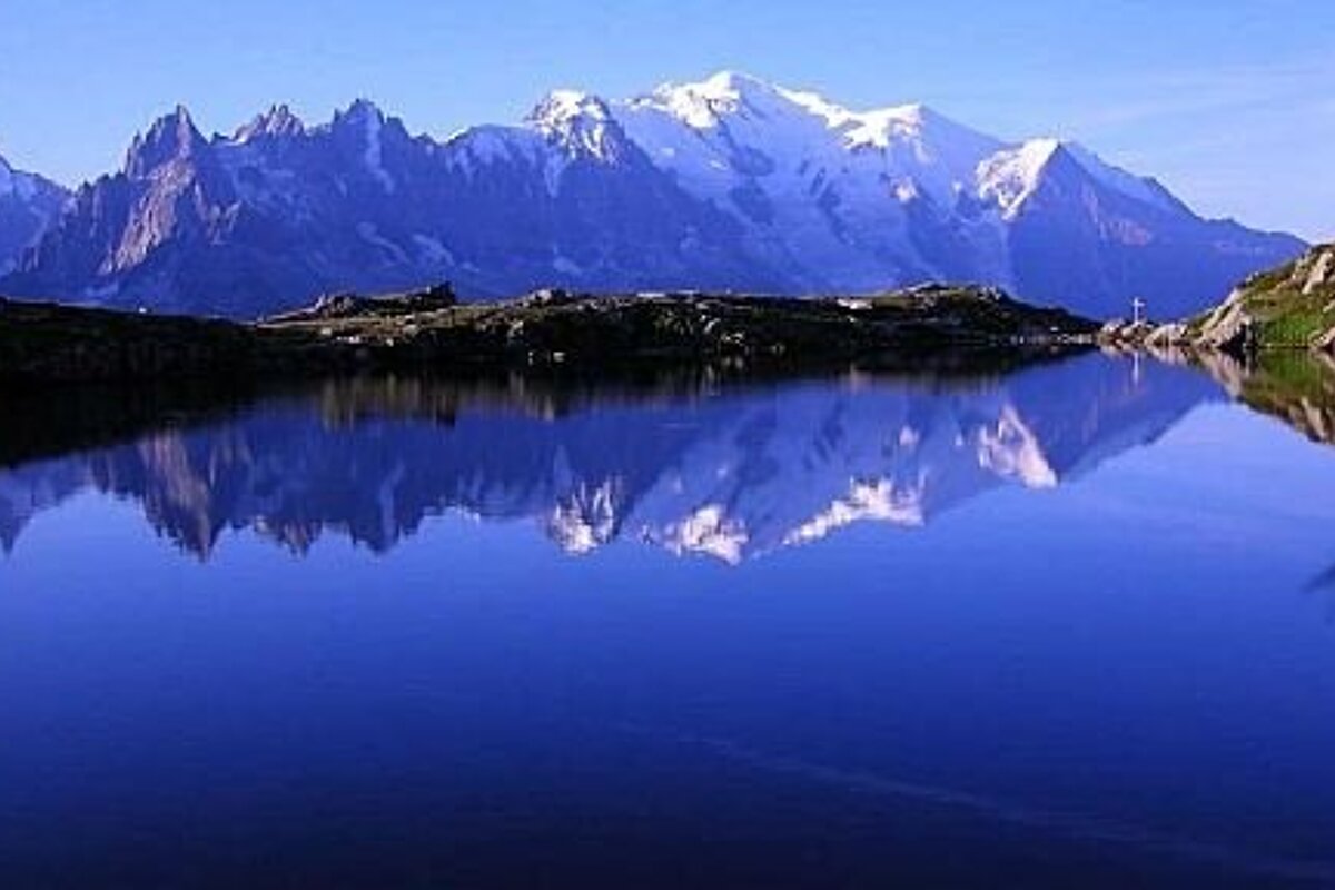 An image of a lake reflecting the mountains in its background with clear blue water. 