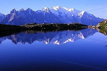 An image of a lake reflecting the mountains in its background with clear blue water.