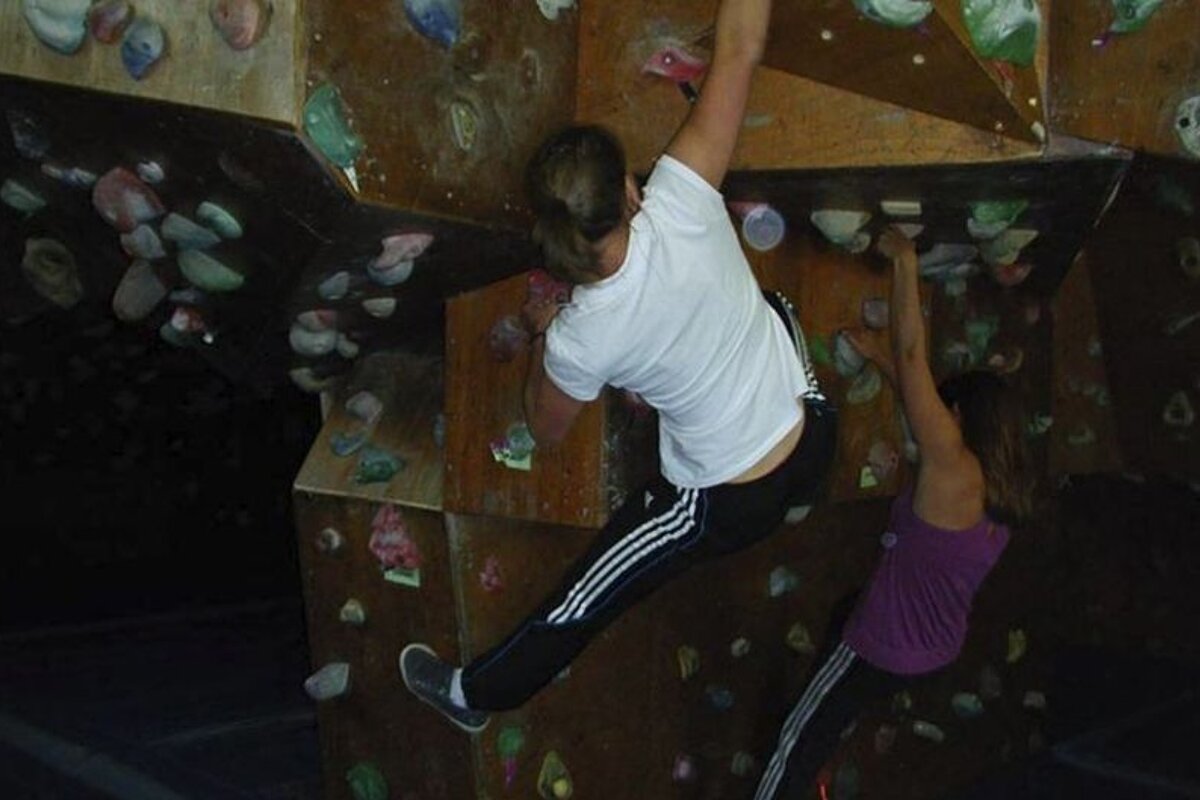 A woman wearing adidas pants climbs a climbing wall