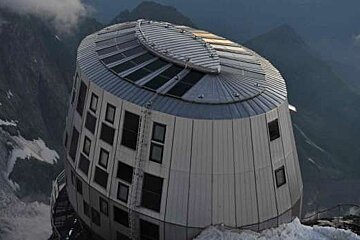 A large round building is sitting on top of a snow covered mountain