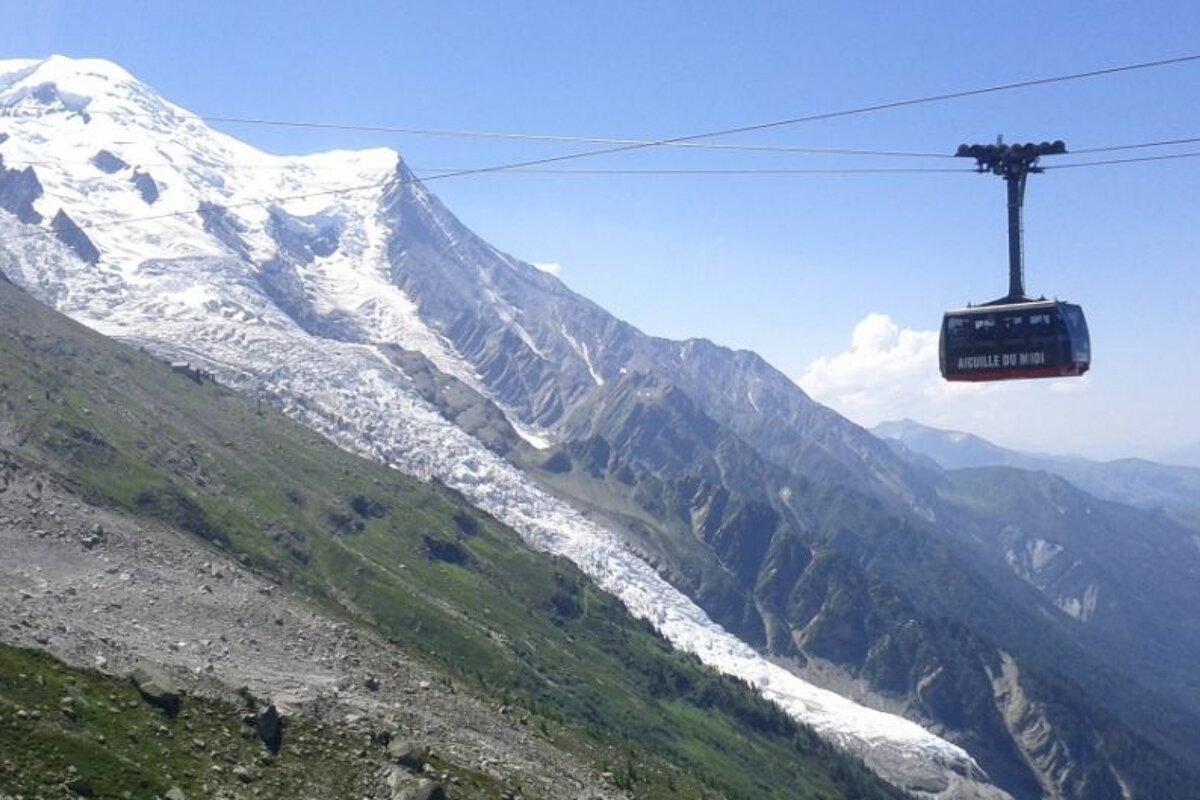 image of the glacier with a cable car suspended in air and the green mountains and blue sky surrouding it.
