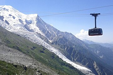 image of the glacier with a cable car suspended in air and the green mountains and blue sky surrouding it.