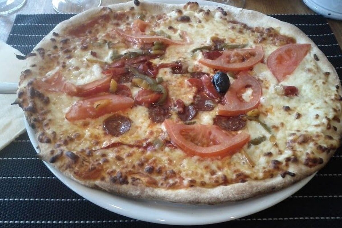 A pizza with tomatoes pepperoni and olives on a white plate