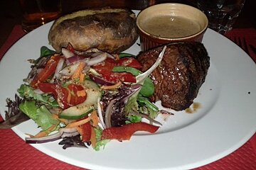 A white plate topped with a steak salad and a baked potato