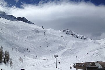 image of a piste with some lifts and runs and people skiing down them with blue sky and a few clouds
