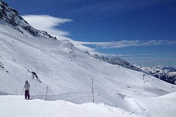 image of a skier skiing on a piste with the mountains and snow in the distance and blue sky above