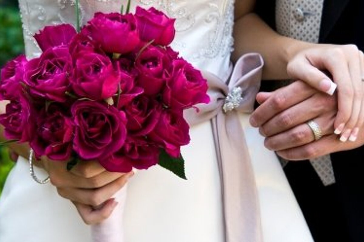 a picture of a bride holding a bunch of roses and holding hands