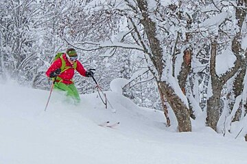 A person in a red jacket and green pants skiing through the snow