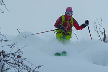 A person in a red jacket and green pants is skiing in the snow