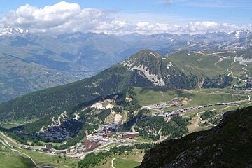 image of a mountain area with a valley below and a town in the valley, green mountains and roads with blue sky and clouds in the distance over the mountains